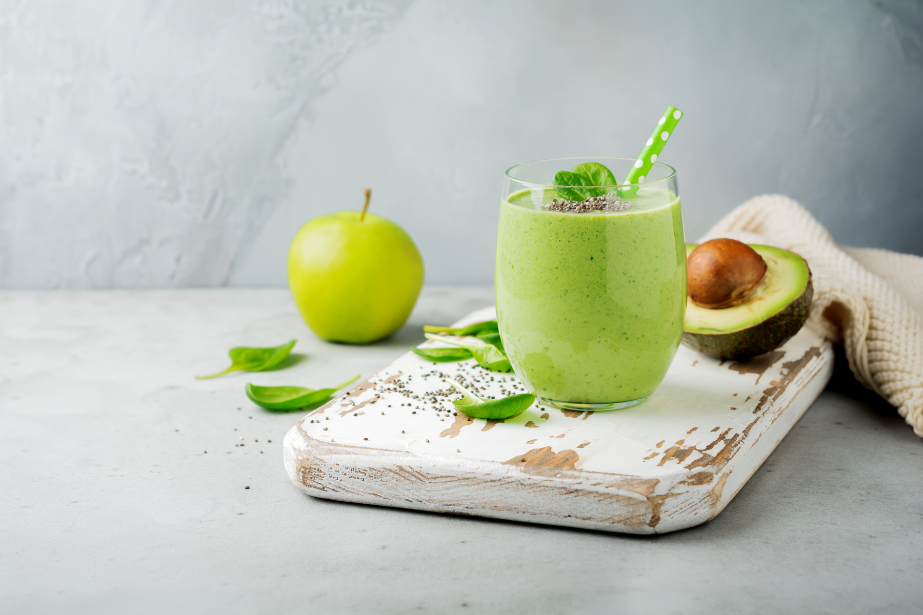 Vegetarian healthy green smoothie from avocado, spinach leaves, apple and chia seeds on gray concrete background. Selective focus. Space for text.